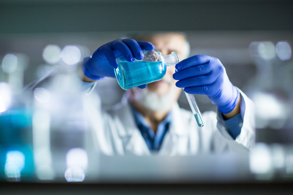 Químico despejando um líquido azul em um pequeno tubo de laboratório como representação da noção de Química.