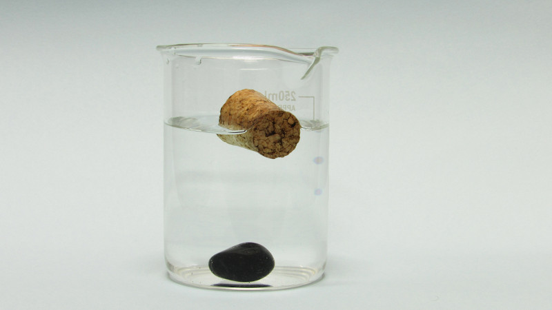 Materiais com diferentes densidades em um copo com líquido transparente.