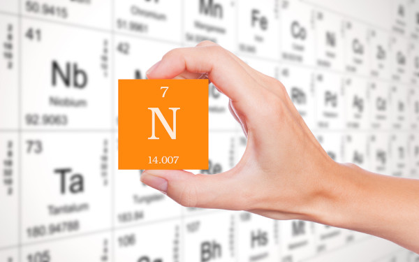 Pessoa segurando um cubo laranja com o símbolo, o número atômico e a massa atômica do nitrogênio.