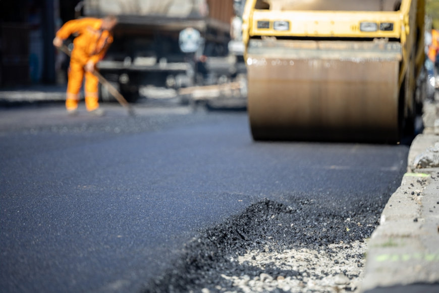 Homem trabalhando junto a uma m&aacute;quina de colocar asfalto, produto feito de alcanos.